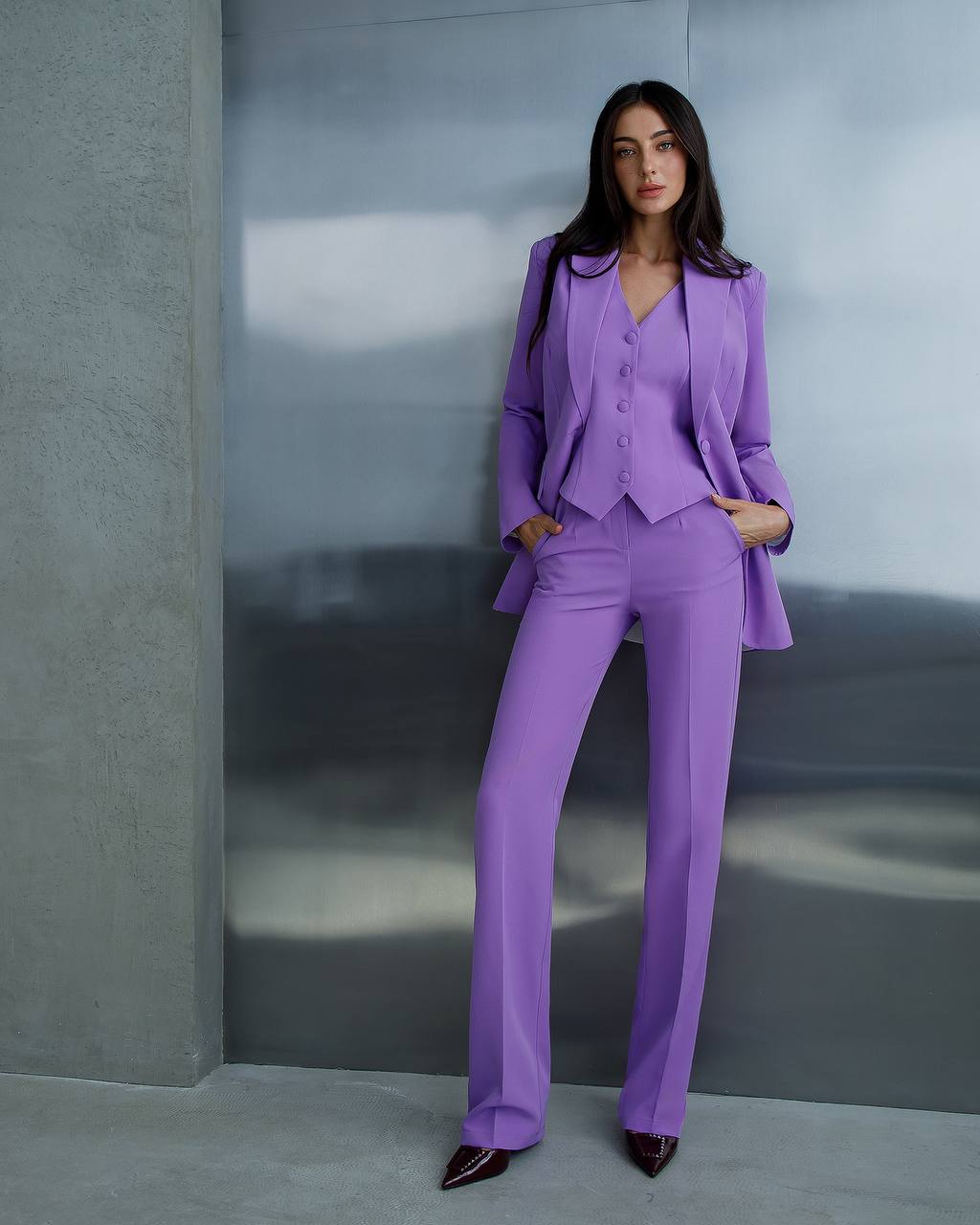 Woman wearing a purple suit standing against a gray wall.