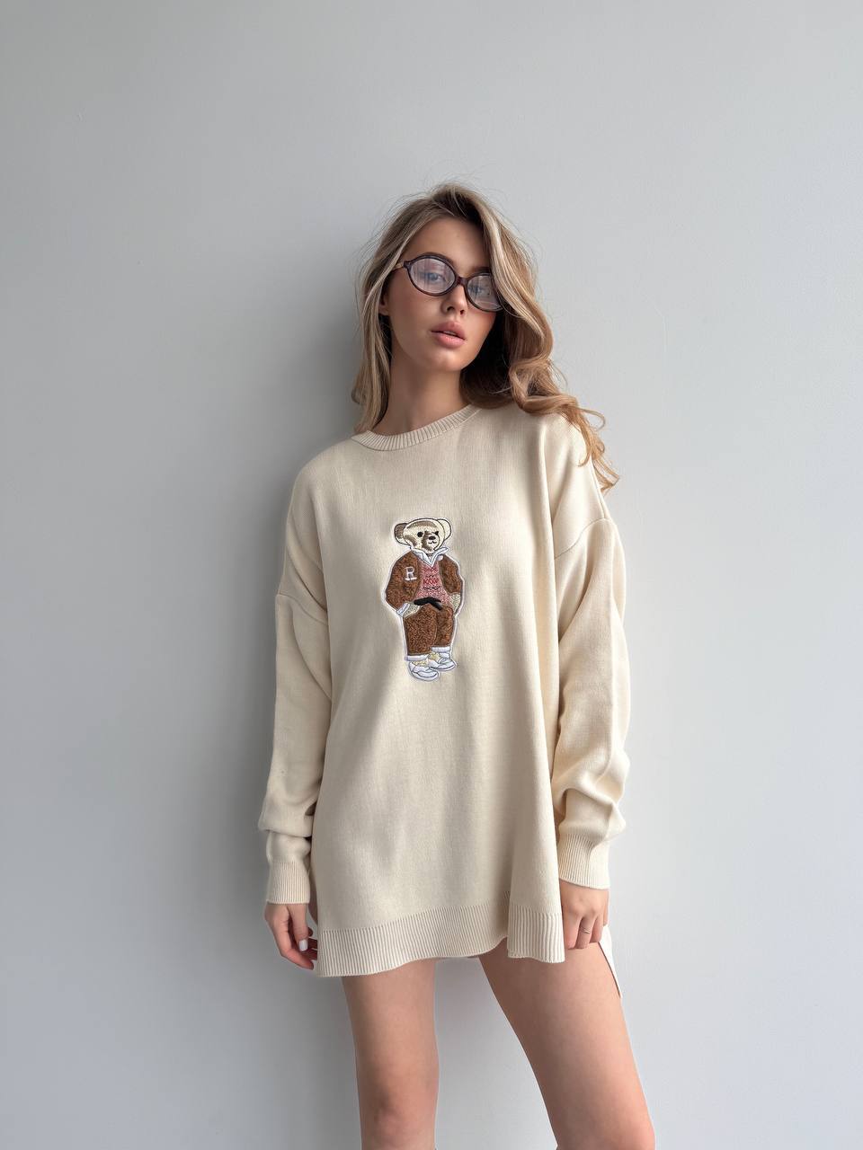 Woman wearing a beige sweatshirt with a graphic design on a plain background