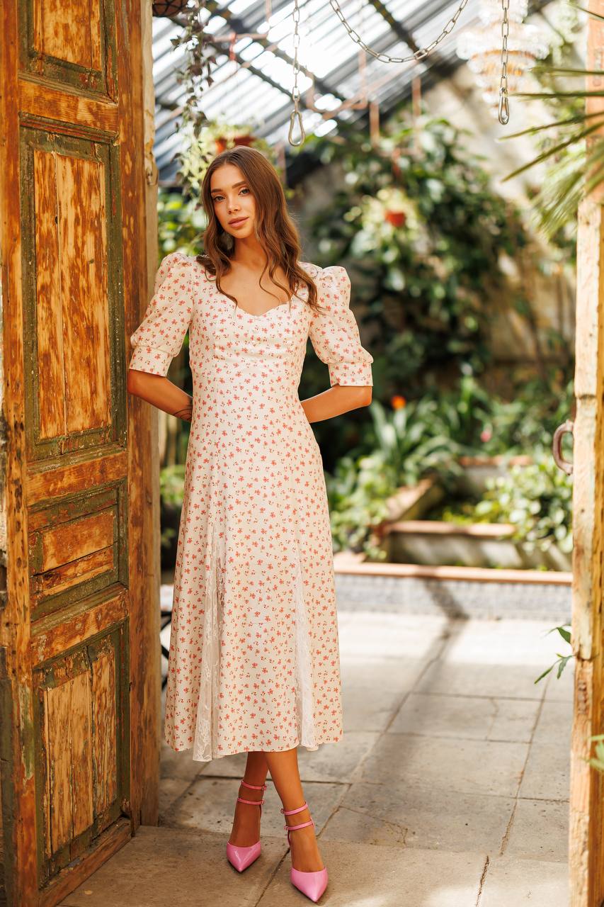 Woman in a floral dress standing in a sunlit greenhouse.