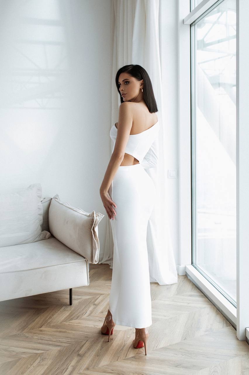 Woman in a white strapless dress standing in a bright room with large windows.