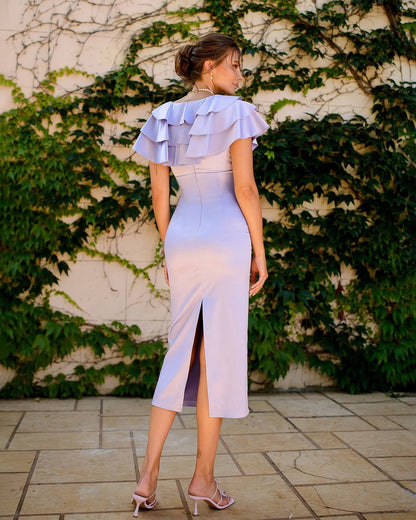Woman wearing a light blue dress with ruffled details, standing against a wall with green ivy.