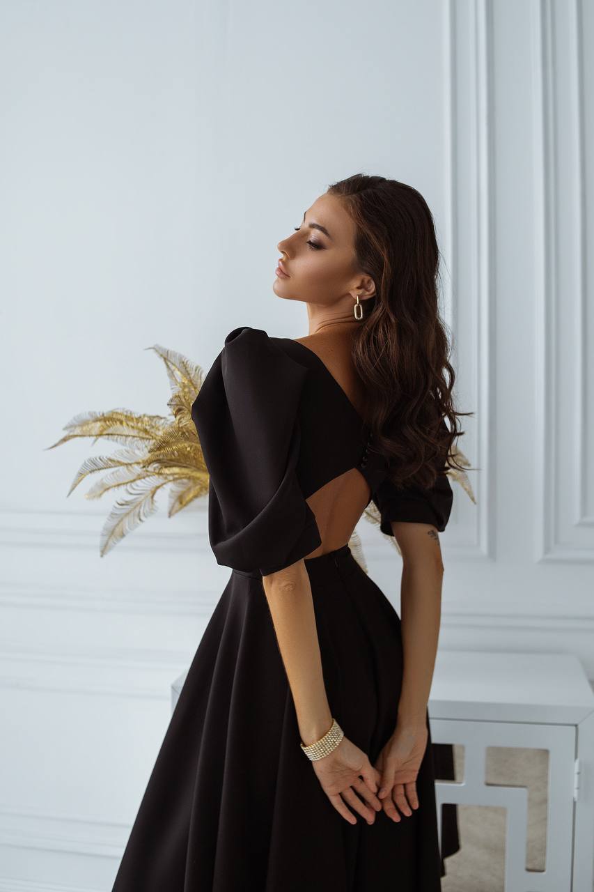 Woman wearing a black dress with a unique back design in an elegant indoor setting.