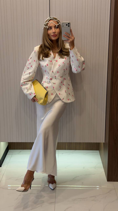 Woman taking a mirror selfie wearing a floral blazer and white pants, holding a yellow bag.