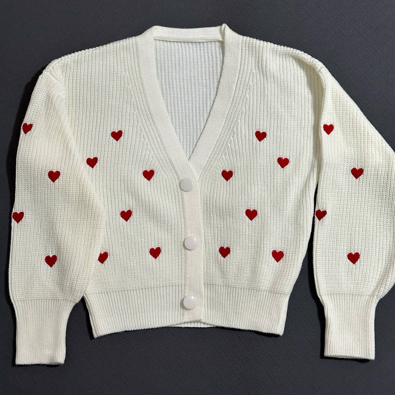 White cardigan with red heart patterns on a dark background