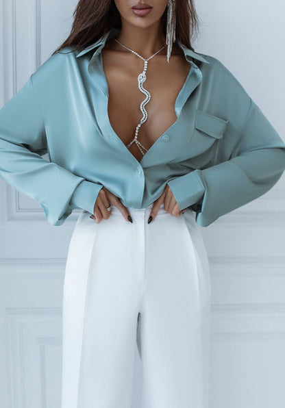 Woman wearing a light blue shirt with a plunging neckline and white pants against a white background
