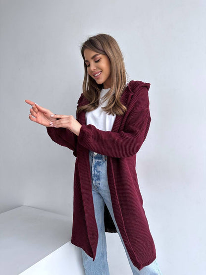 Woman wearing a burgundy cardigan over a white shirt and blue jeans on a plain background