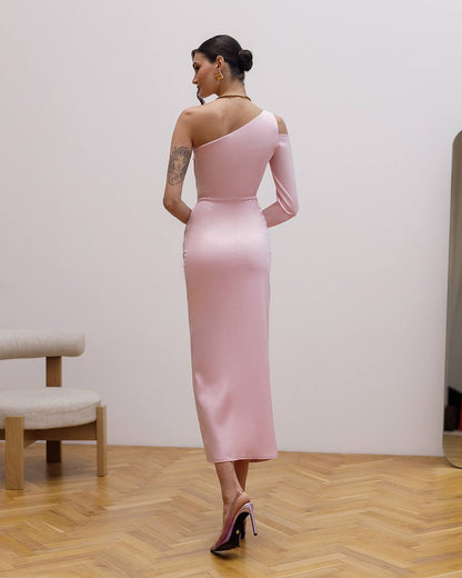 Woman in a pink one-shoulder dress standing in a room with wooden floor and white wall.