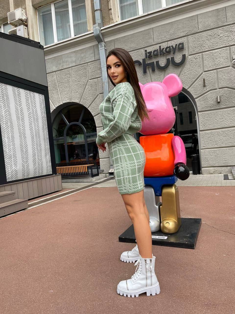 Woman in a green outfit standing in front of colorful bear sculptures and an izakaya restaurant.