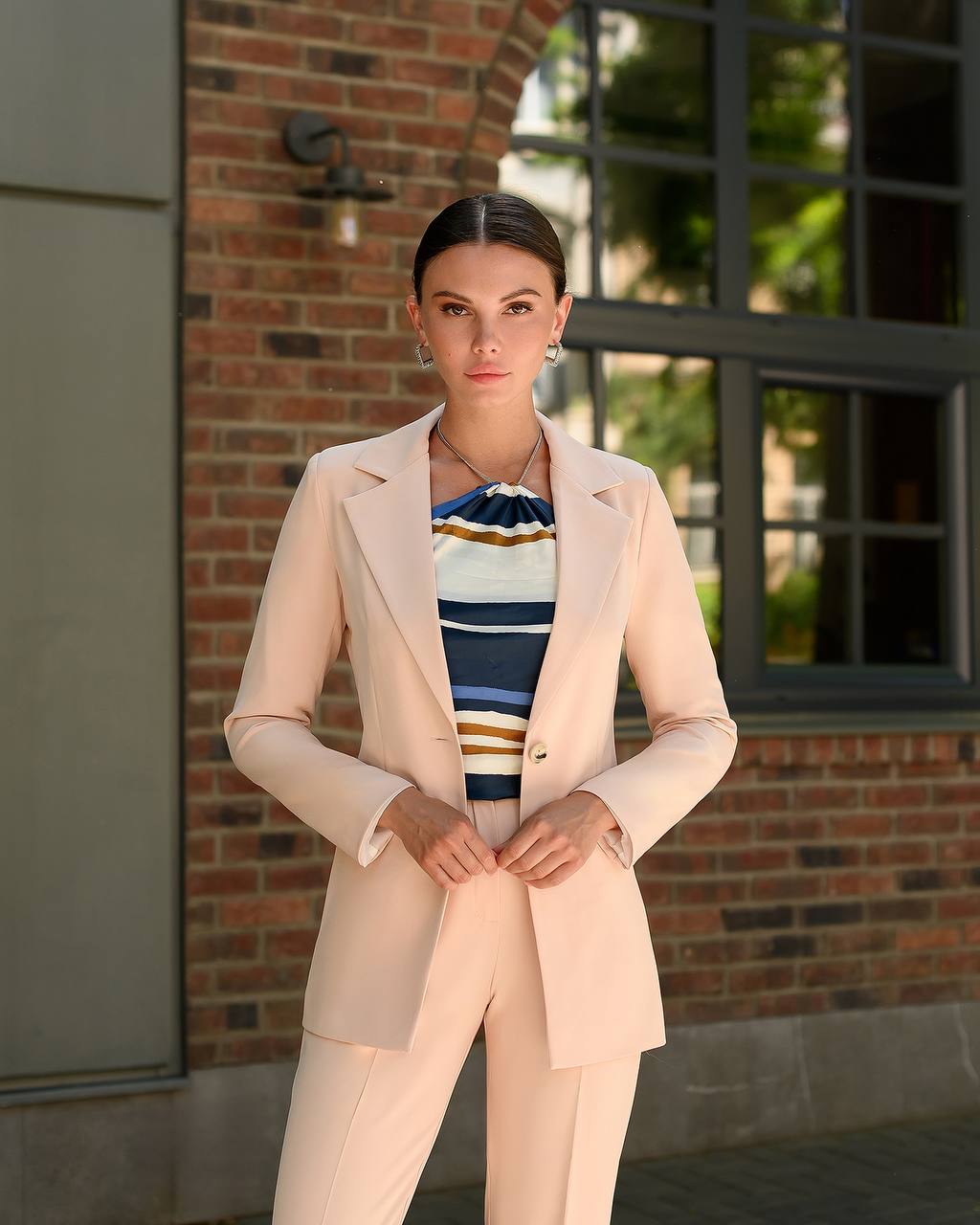 Woman in a beige suit standing in front of a brick wall
