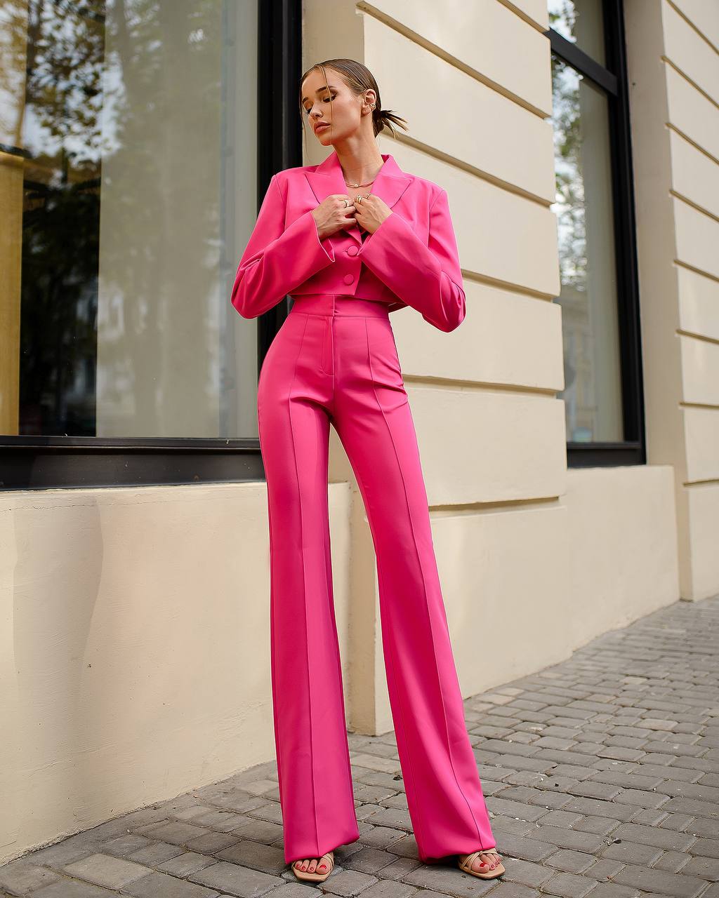 Woman in a bright pink suit standing outside a building.