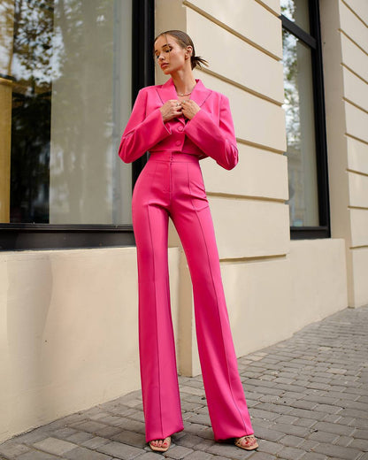 Woman in a bright pink suit standing outside a building.