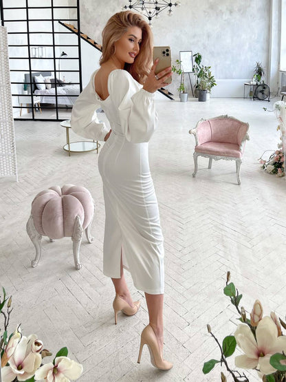 Woman in a white dress taking a selfie in a stylish room with pink furniture and floral decorations.