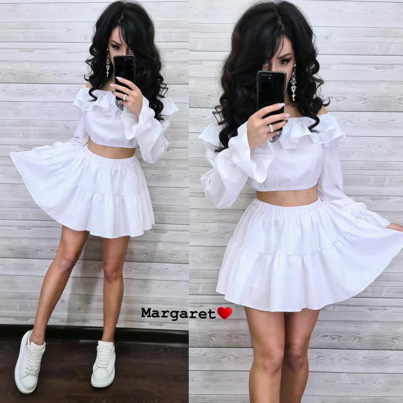 Person wearing a white outfit with ruffled sleeves and a skirt, standing against a wooden panel background.