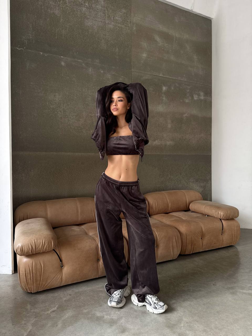 Woman in dark athletic wear standing in a modern room with a brown sofa.