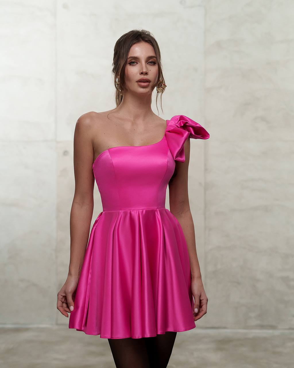 Woman wearing a bright pink one-shoulder dress against a neutral background