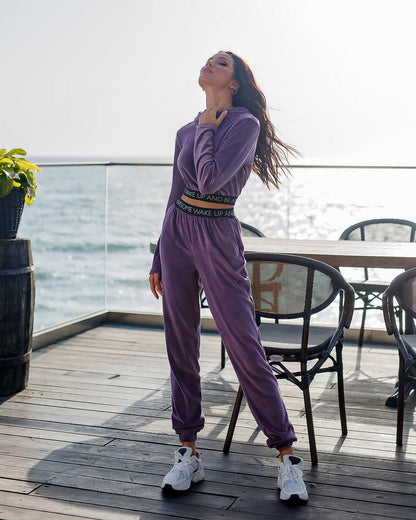 Woman in a purple tracksuit standing on a wooden deck by the water.