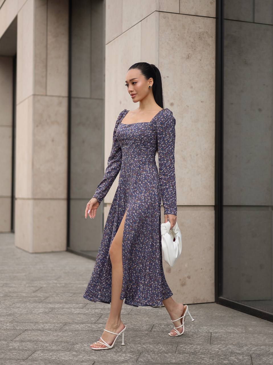 Woman in a purple floral dress with a high slit walking outdoors.