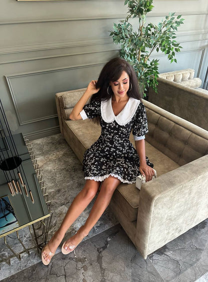 Woman in a floral dress sitting on a couch in an indoor setting