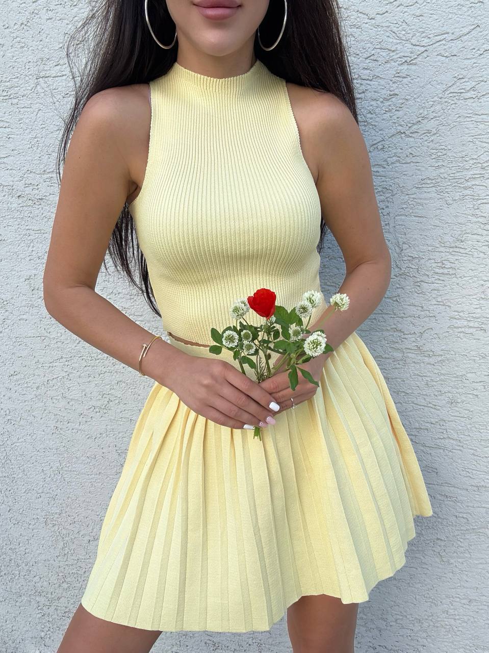Woman in a yellow dress holding flowers against a gray wall
