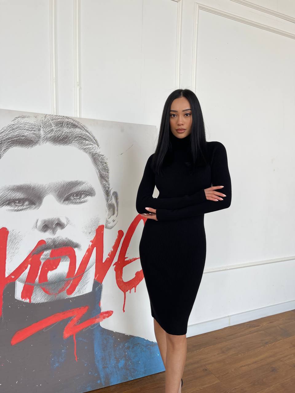 Woman in a black dress standing in front of a large abstract painting with bold red text.