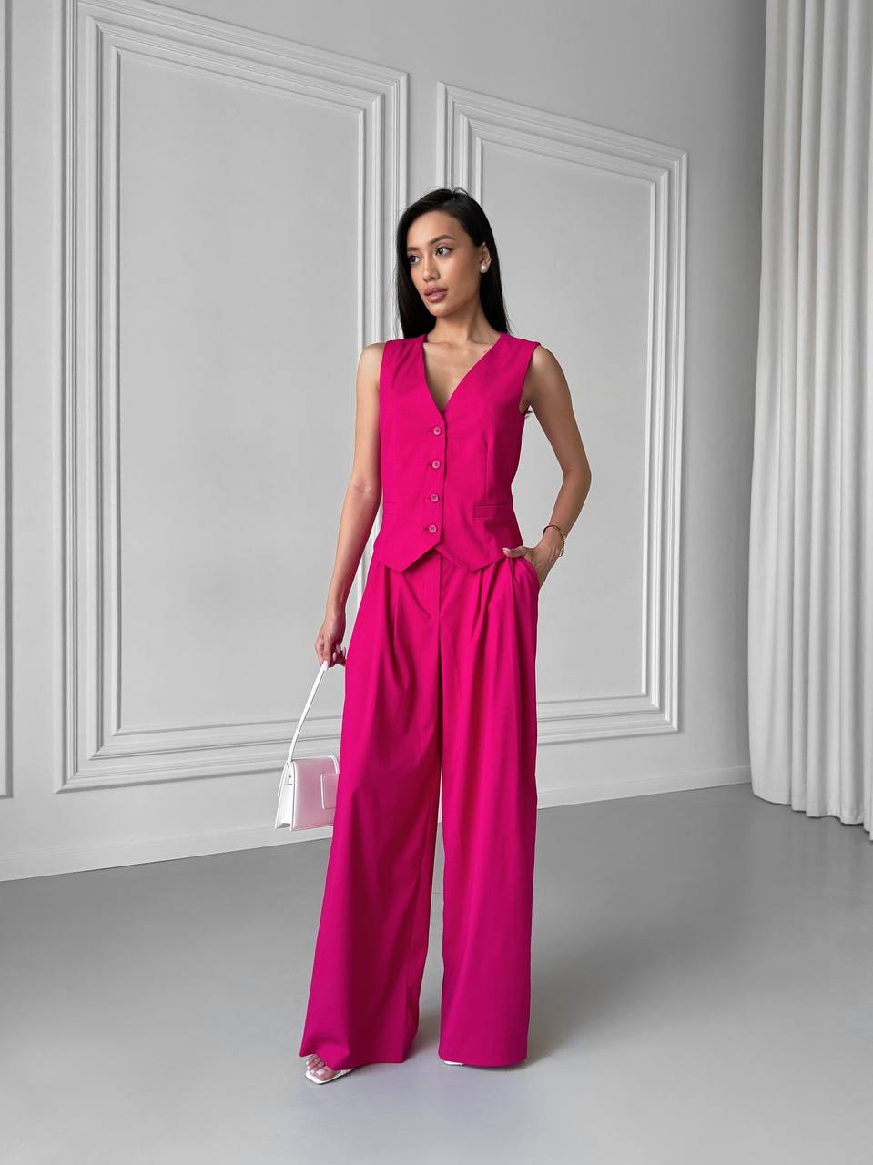 Woman wearing a bright pink jumpsuit against a gray wall.