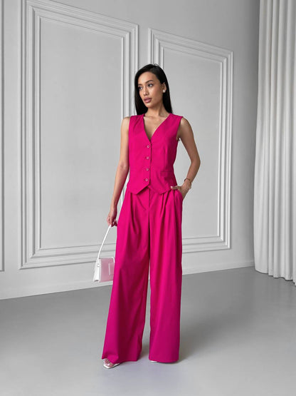 Woman wearing a bright pink jumpsuit against a gray wall.