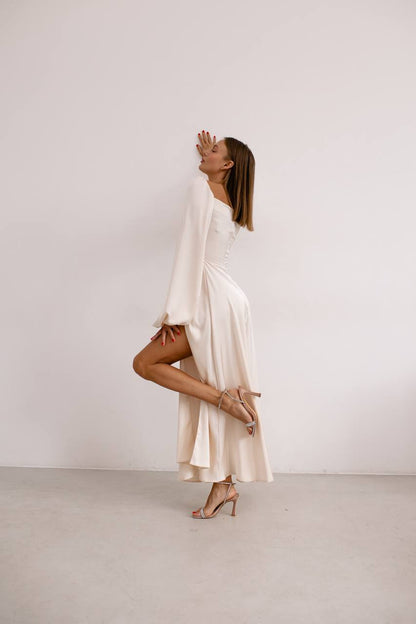 Woman in a white dress standing on one leg against a plain background