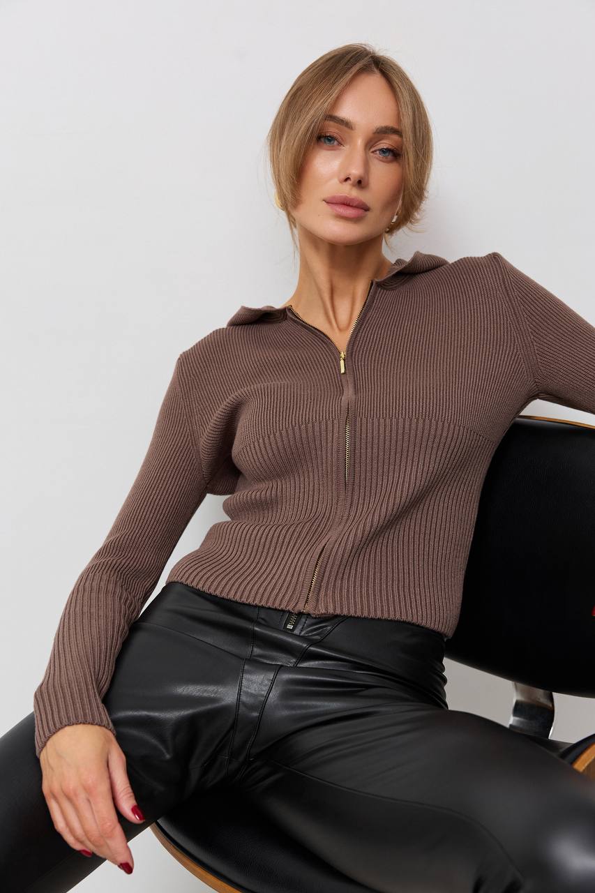 Woman wearing a brown ribbed sweater and black leather pants sitting on a chair.