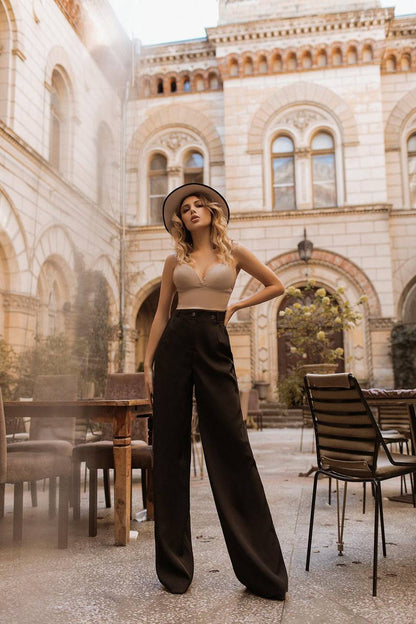 Woman posing in a stylish outfit with a hat in an outdoor setting with tables and chairs.