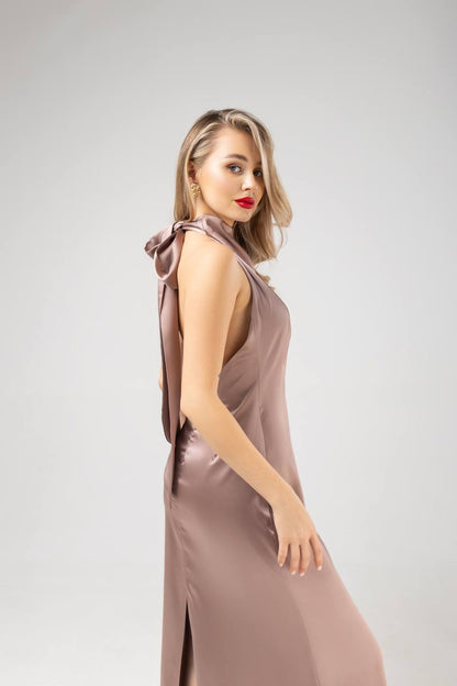 Woman wearing a long, elegant dress with a bow detail on a plain background