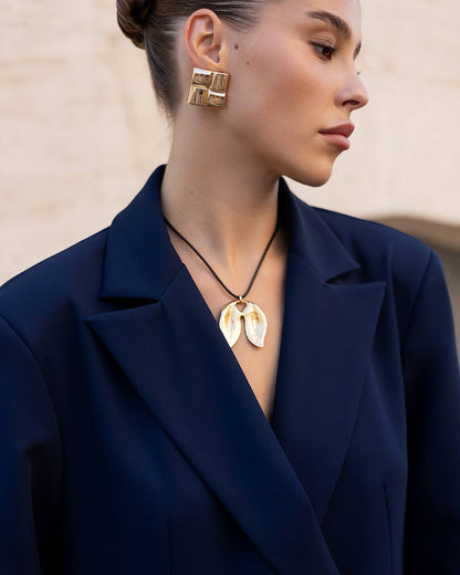 Woman wearing gold earrings and necklace against a neutral background