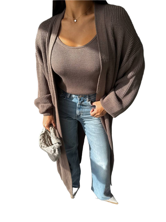 Woman wearing a brown cardigan, beige top, and blue jeans on a white background