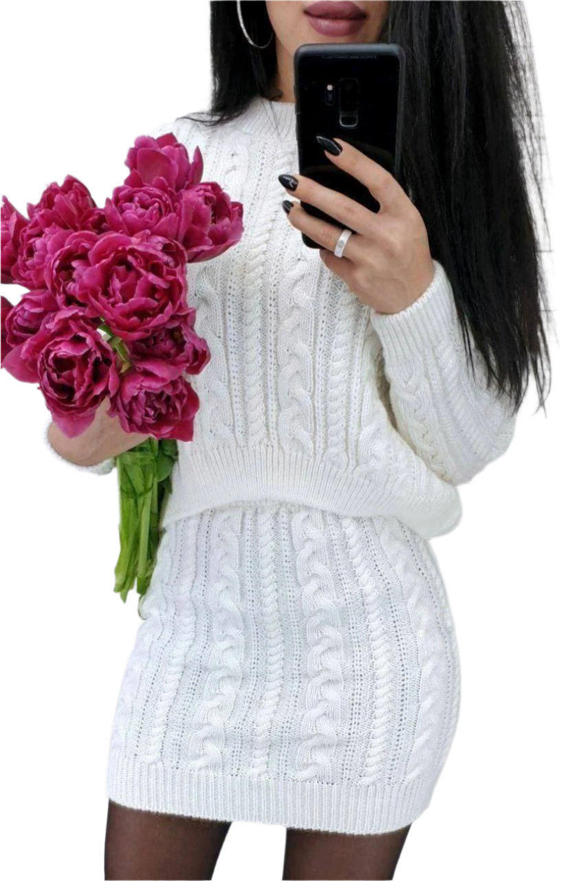 Person wearing a white cable knit sweater and skirt holding pink flowers and a phone.