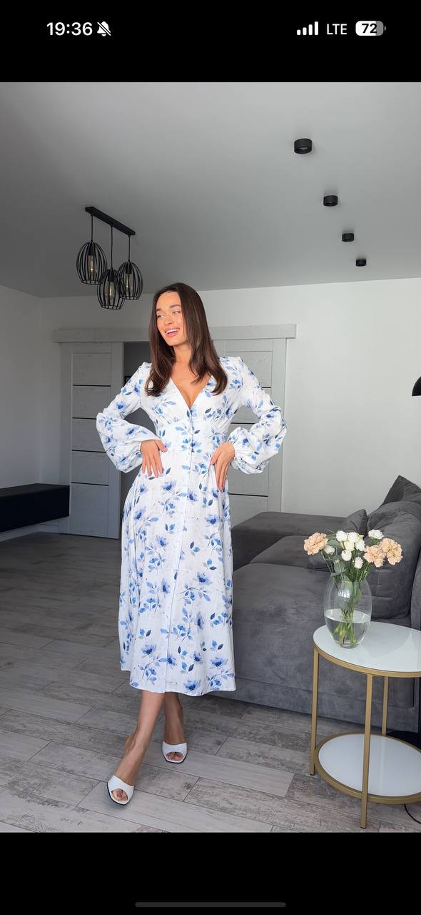 Woman in a floral dress standing in a modern living room.