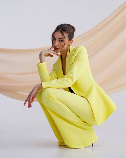 Woman in a bright yellow suit sitting on a white floor with a beige fabric draped behind her.