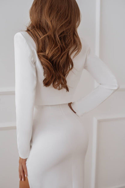 Woman wearing a white dress with long sleeves against a white wall