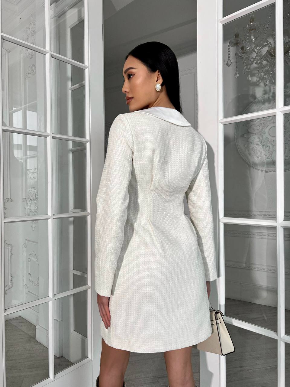 Woman in a white dress standing in a doorway with a neutral background