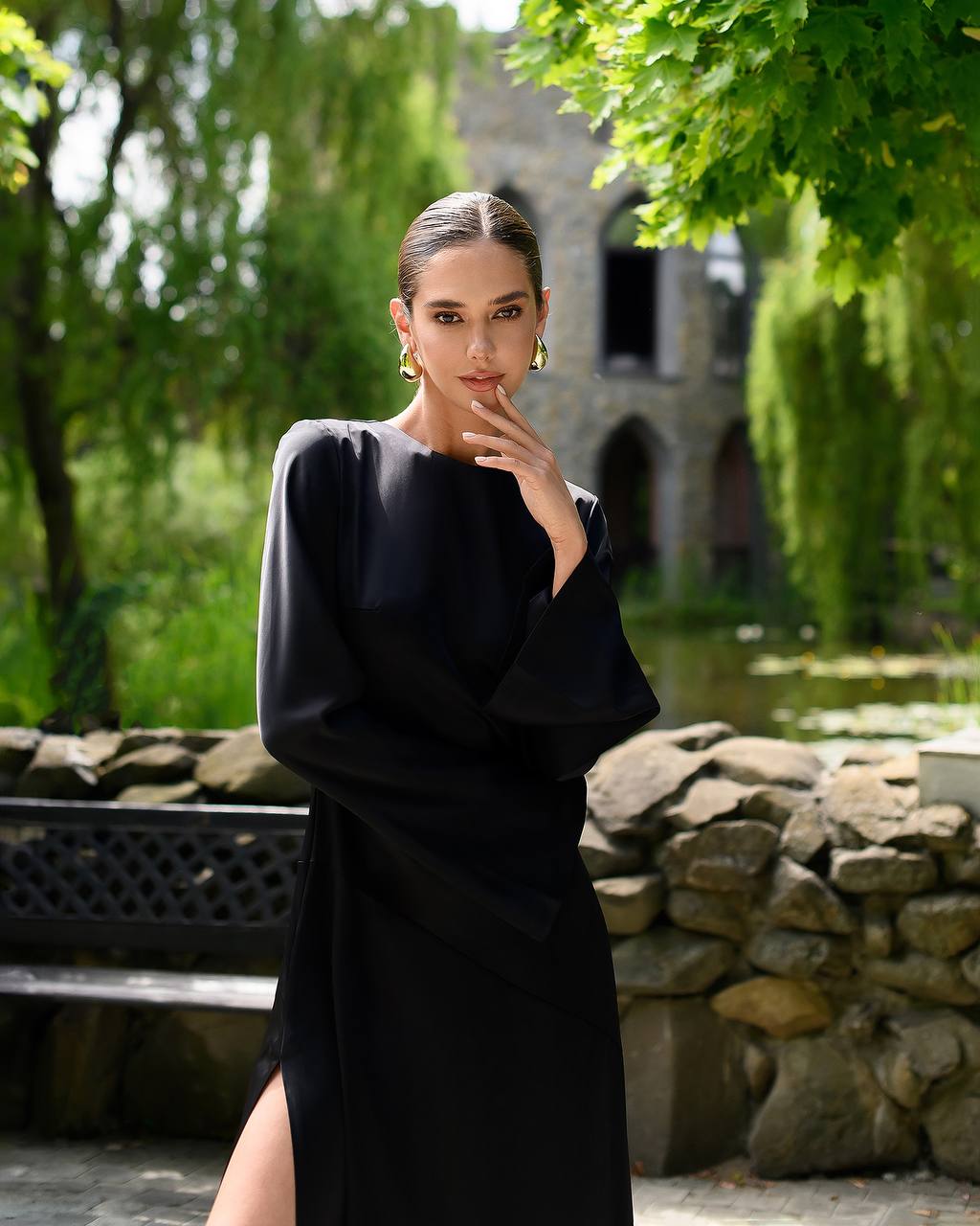 Woman in a black dress standing in a garden with stone walls and greenery.