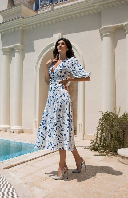 Woman in a white dress with blue patterns standing by a poolside.
