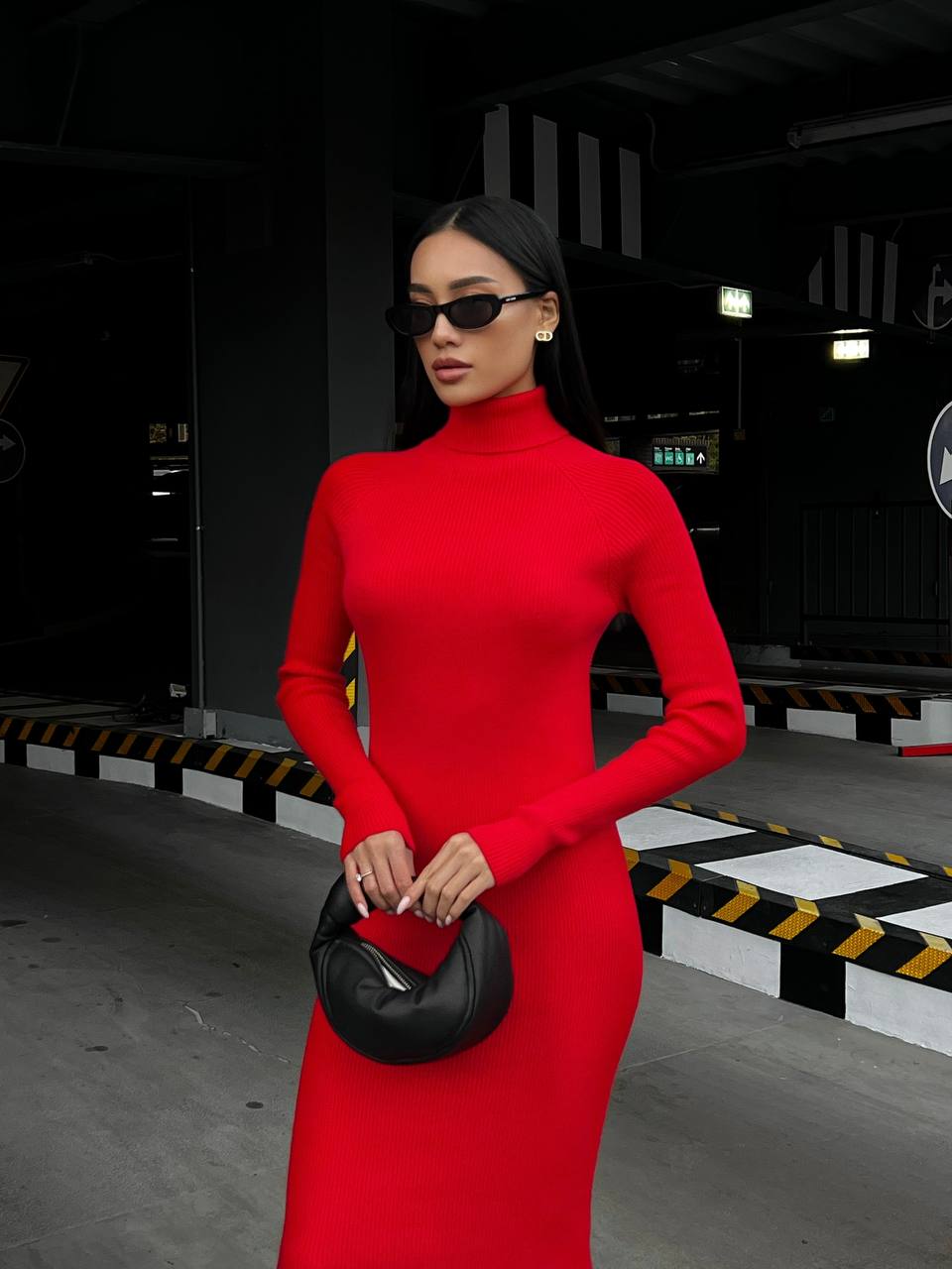 Woman in a red dress holding a black handbag in an industrial setting