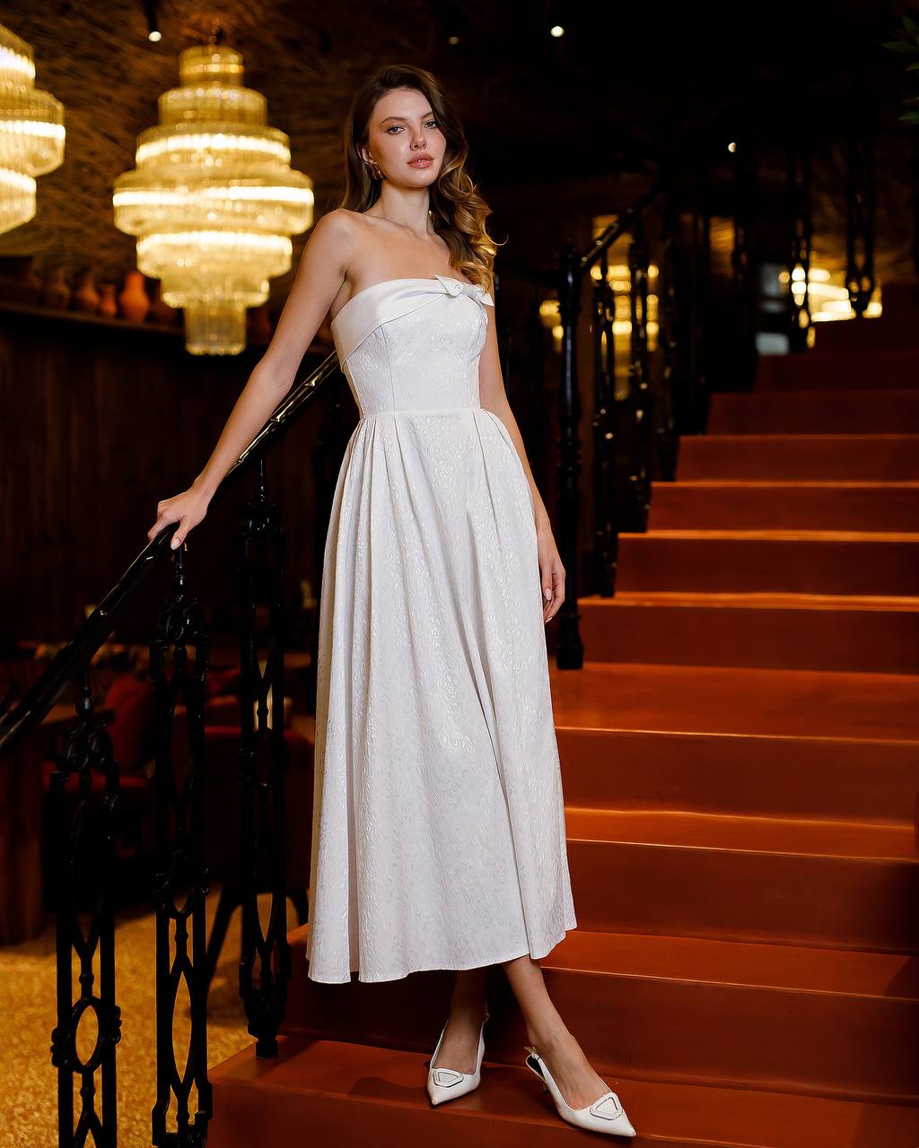 Woman in a white dress standing on a staircase in an elegant interior setting