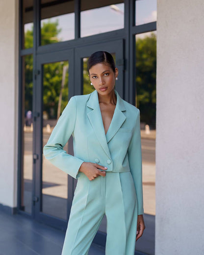 Woman in a light blue suit standing in front of a building entrance.