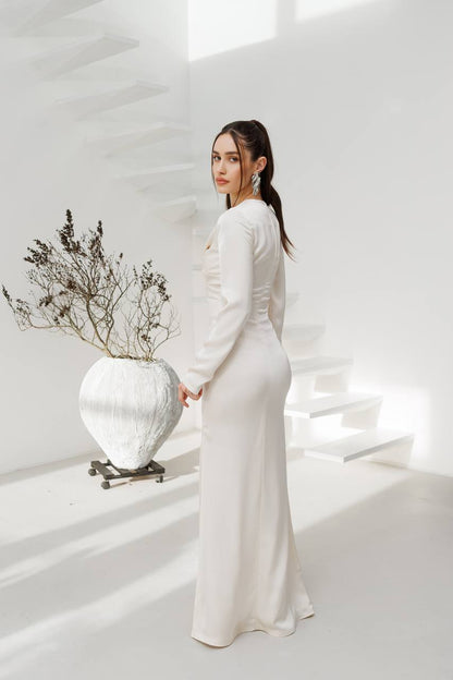 Woman in a white dress holding a white vase with dried plants against a white background