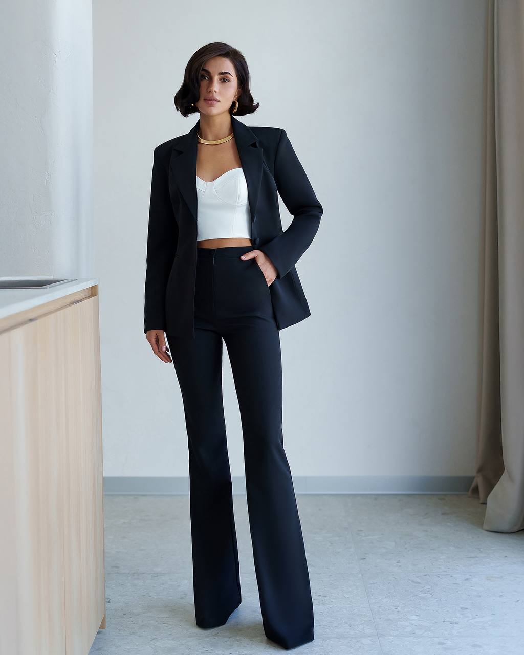 Woman wearing a black suit with a white top in a minimalistic room.