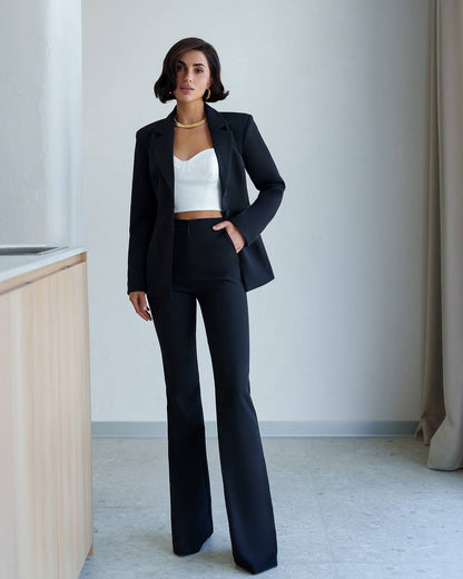 Woman wearing a black suit with a white top in a minimalistic room.