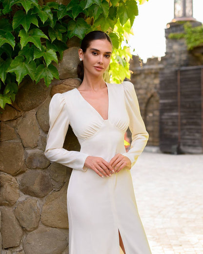 Woman in a white dress standing against a stone wall with greenery