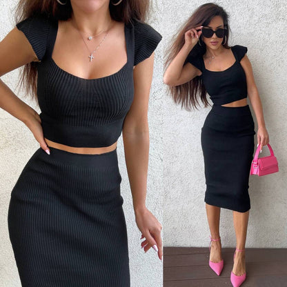 Woman wearing a black ribbed outfit with pink shoes and a pink handbag against a neutral background.