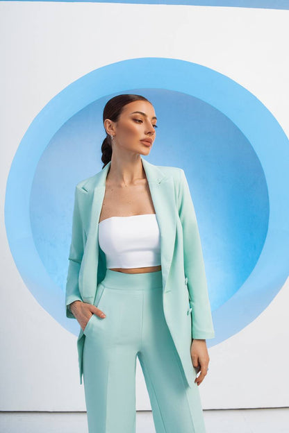 Woman in a light green suit standing against a white background with blue circular design
