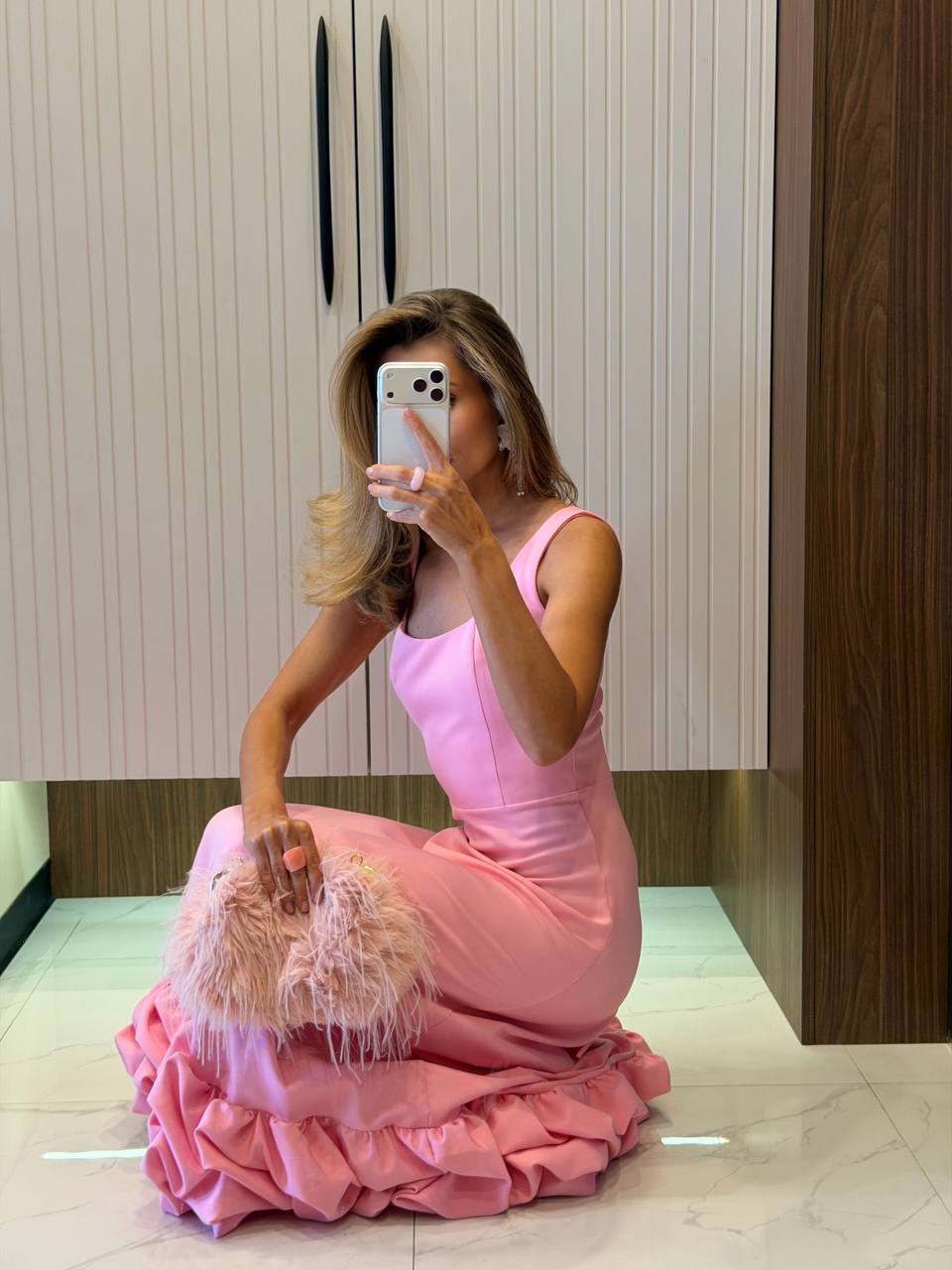 Woman in a pink dress taking a mirror selfie in an indoor setting.