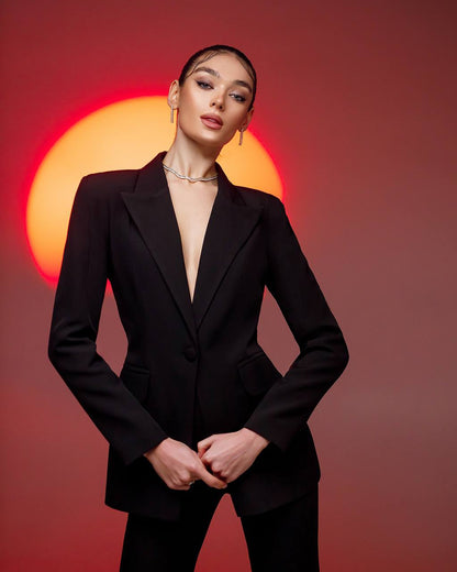 Woman wearing a black suit against a red background with a sun-like light source.